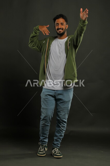 التعابير والرقصات بالاحتفالات والمناسبات في المملكة, رقصات سعودية تقليدية شعبية, العراقة والأصالة والتراث السعودي, بورتريه لرجل عربي خليجي سعودي يرتدي الزي الكاجوال يرفع يديه للأعلى, صورة الجسم بالطول الكامل, خلفية رمادية