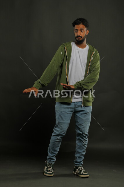 رفع اليدين بإيماءات الاحتياط والقلق والتوقف , طلب الابتعاد وعدم الاقتراب, حماية النفس من ضرر خارجي, بورتريه لرجل عربي خليجي سعودي يرتدي الزي الكاجوال و يقف بحذر, صورة الجسم بالطول الكامل, خلفية سوداء
