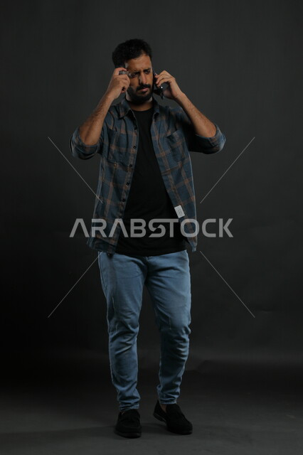 التفكير والتأمل والخطيط للمستقبل، بورتريه لرجل أعمال عربي  سعودي خليجي يرتدي الزي الكاجوال يجري مكالمة هاتفيه، تشاور ومحادثات باستخدام الهاتف المحمول، إيماءات التركيز وإيجاد حل لمشكلة ما، صورة الجسم بالطول الكامل، خلفية سوداء .