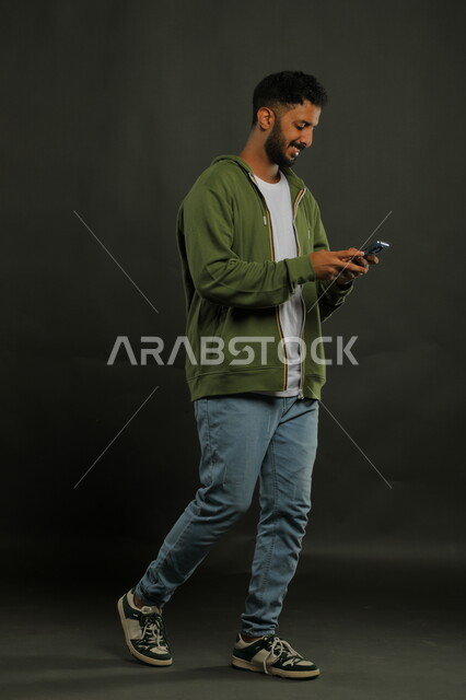 Using modern devices to develop personal skills, professionalizing technical and information technology jobs, following the latest social media news, a portrait of a smiling Saudi Arab Gulf man wearing casual clothes using a mobile phone, full body portrait, black background