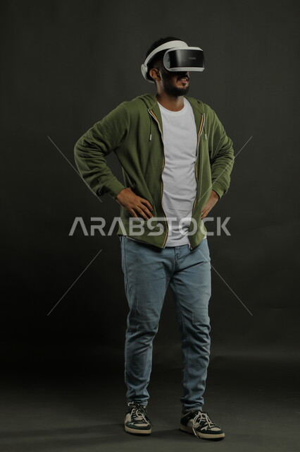 Advanced devices and technologies, integration with virtual reality movies, placing hands on the waist with waiting gestures, simulating the imaginary world, portrait of a Saudi Gulf Arab man wearing casual clothes and 3D VR glasses, full-length body portrait, black background