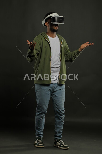 مشاهدة الأفلام المفضلة بإيماءات التساؤل والاستفهام،محاكاة العالم الخيالي, بورتريه لشاب عربي سعودي خليجي يرتدي الزي الكاجوال ونظارة في آر ثلاثية الأبعاد يرفع يديه  للاعلى , التفاعل والاندماج مع ألعاب الواقع الافتراضي, صورة الجسم بالكامل, خلفية سوداء .