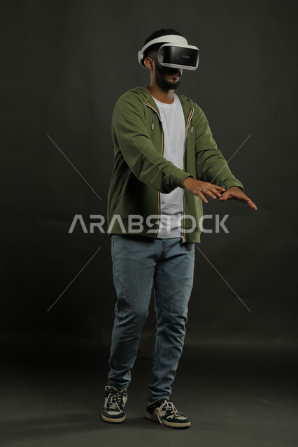 استخدام التقنيات الحديثة المتطورة، الاندماج ومحاولة امساك شيء ما, التفاعل ومحاكاة العالم الخيالي, بورتريه لشاب عربي خليجي سعودي يرتدي الزي الكاجوال يقوم بمشاهدة الأفلام عبر نظارة الواقع الافتراضي ثلاثية الأبعاد, صورة الجسم بالطول الكامل, خلفية سوداء