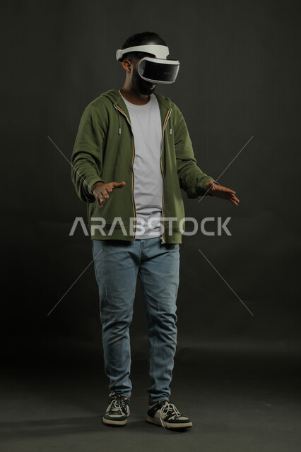 Advanced technologies and devices, enjoying the simulation of the imaginary world, a portrait of a Saudi Gulf Arab man wearing casual clothes and 3D VR glasses looking down and trying to touch an item, interacting and merging with virtual reality games, a portrait of the full body, black background
