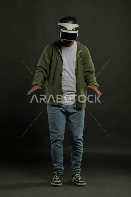 الاستمتاع في محاكاة العالم الخيالي، بورتريه لرجل عربي سعودي خليجي يرتدي الزي الكاجوال ونظارة في آر ثلاثية الأبعاد ينظر للأسفل ومحاولة لمس عنصر ما , التفاعل والاندماج مع ألعاب الواقع الافتراضي, تقنيات وأجهزة متطورة, صورة الجسم بالطول الكامل, خلفية سوداء