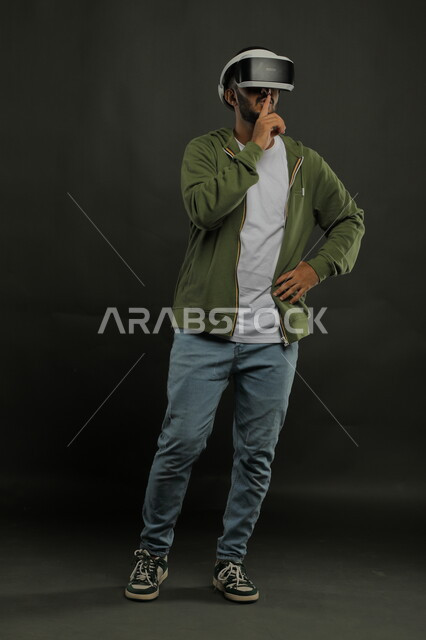 ايماءات طلب السكوت والتوقف عن الكلام، التفاعل والاندماج ومحاكاة العالم الخيالي, التسلية والترفيه والمتعه في أوقات الفراغ , بورتريه لرجل عربي خليجي سعودي يرتدي الزي الكاجوال ونظارة الواقع الافتراضي ويشاهد الافلام المفضلة , صورة الجسم بالكامل, خلفية سوداء