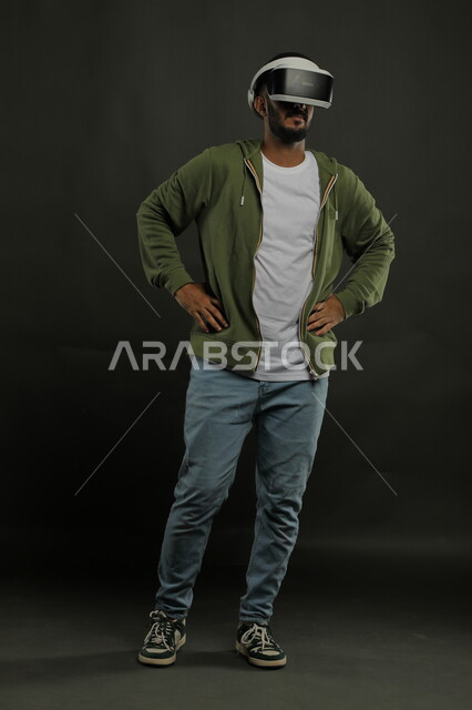Integration with virtual reality movies, placing hands on the waist with waiting gestures, simulating the imaginary world, portrait of a Saudi Gulf Arab man wearing casual clothes and 3D VR glasses, advanced technologies and devices, full-length body portrait, black background