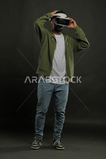 التفاعل والاندماج ومحاكاة العالم الخيالي, التسلية والترفيه والمتعه في أوقات الفراغ , بورتريه لرجل عربي خليجي سعودي يرتدي الزي الكاجوال ونظارة الواقع الافتراضي ويشاهد الافلام المفضلة , صورة الجسم بالكامل, خلفية سوداء