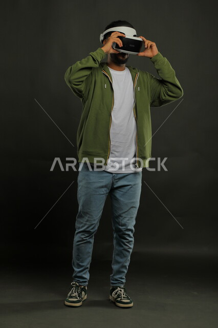 التسلية والترفيه والمتعه في أوقات الفراغ ،التفاعل والاندماج ومحاكاة العالم الخيالي, بورتريه لرجل عربي خليجي سعودي يرتدي الزي الكاجوال ونظارة الواقع الافتراضي ويشاهد الافلام المفضلة , صورة الجسم بالكامل, خلفية سوداء