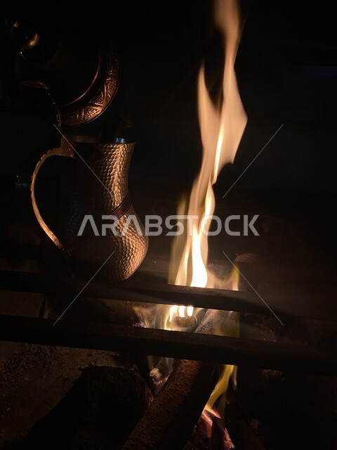صورة مقربة لدلة قهوة عربيه معدنية بجانب شبة النار ليلا, ,تناول المشروبات الساخنة في الأجواء الشتوية الباردة, جلسات بدوية شعبيه في صحاري المملكة العربية السعودية