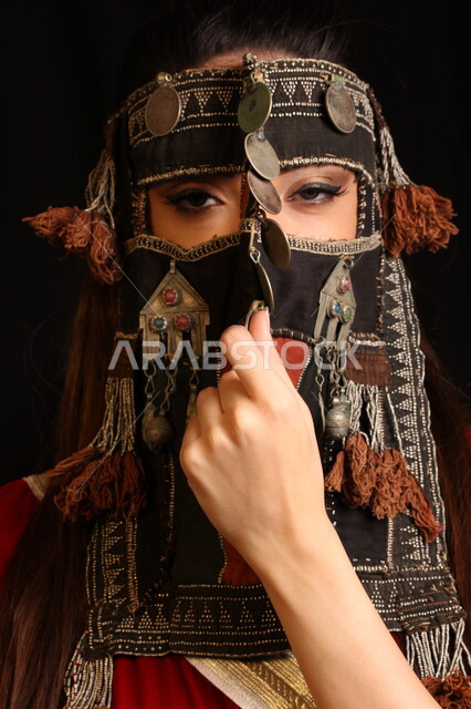 احياء ذكرى المناسبات الوطنية التاريخية، الأناقة والاهتمام بالمظهر الخارجي، بورتريه مقرب لفتاة عربية سعودية خليجية ترتدي برقع قديم مطرز و مزخرف بالعملات المعدنية تنظر إلى الكاميرا، تأسيس الدولة السعودية الأولى ١٧٢٧، يوم التأسيس ٢٢ فبراير، خلفية سوداء.