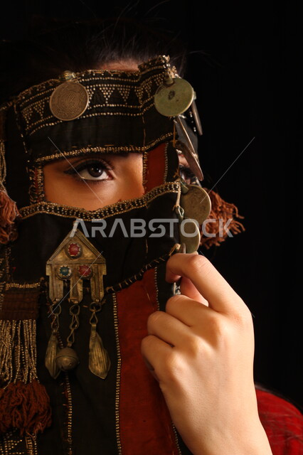 الأناقة والاهتمام بالمظهر الخارجي، بورتريه مقرب لفتاة عربية سعودية خليجية ترتدي برقع قديم مطرز و مزخرف بالعملات المعدنية، تأسيس الدولة السعودية الأولى ١٧٢٧، احياء ذكرى المناسبات الوطنية التاريخية، يوم التأسيس ٢٢ فبراير، خلفية سوداء.