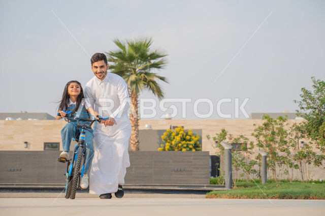 ايماءات الحماس والسرور، قضاء اوقات عائلية ممتعة في وقت العطلة الصيفية, ممارسة رياضة ركوب الدراجات الهوائيه, فتاة عربية خليجية سعودية تقوم بقيادة الدراجة بمساعدة شقيقها في إحدى الحدائق العامة, أنشطة ترفيهيه مسلية, منتجعات وشاليهات راقية في السعودية