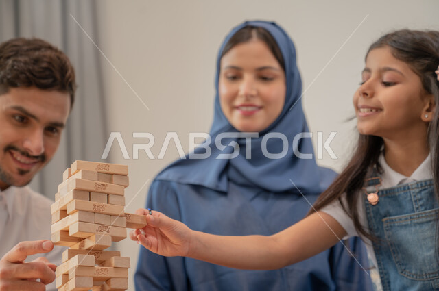 قضاء إجازة ممتعة في اللعب مع الأبناء، صورة مقربة لعائلة عربية خليجية سعودية مبتسمة تلعب لعبة جينغا بإيماءات الفرح، رص الألواح الخشبية، أنشطة ترفيهية لتنمية مهارات التفكير والذكاء عند الأطفال، ألعاب عائلية مسلية.