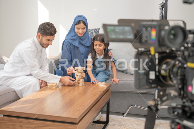 قضاء إجازة ممتعة في اللعب مع الأبناء بألعاب التحدي المسلية، خلف الكواليس لجلسة تصوير في غرفة المعيشة لعائلة عربية خليجية سعودية تلعب لعبة جينغا، لقطة مقربة لكاميرا حديثة ومتطورة, رص الألواح الخشبية، إيماءات الاندماج بالتسلية والترفيه .