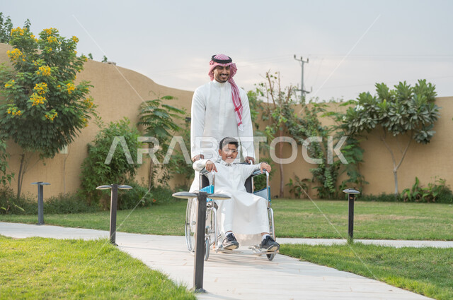 الشقق والفلل السكنية الفاخرة ،أدوات تساعد مرضى ذوي الإعاقة الحركية على التنقل بسهولة, تحسين حياة أصحاب الهمم وتأمين احتياجاتهم الخاصة, رجل عربي خليجي سعودي يرتدي الزي التقليدي برفقة ابنه في إحدى الحدائق، ولد سعودي مبتسم مقعد يجلس على كرسي متحرك بإيماءات السرور