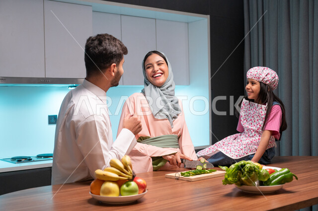 Skills and arts of cooking and cutting, the concept of a healthy diet, spending enjoyable times with the children, gestures of happiness and pleasure in cooperation between family members in the kitchen, a veiled Saudi Arabian Gulf mother teaching her daughter to cook, preparing and preparing food with fresh natural ingredients.