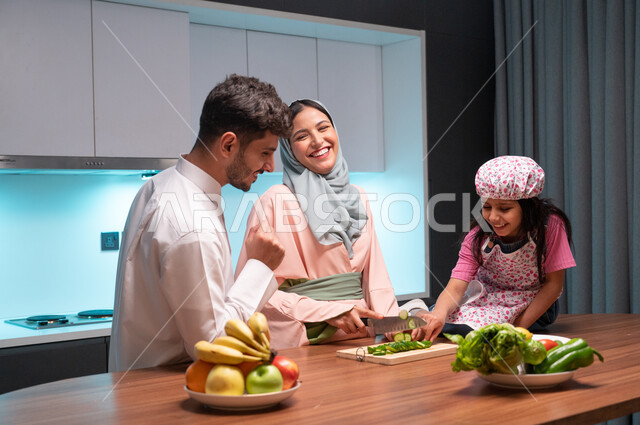 Skills and arts of cooking and cutting, the concept of a healthy diet, spending enjoyable times with the children, gestures of happiness and pleasure in cooperation between family members in the kitchen, a veiled Saudi Arabian Gulf mother teaching her daughter to cook, preparing and preparing food with fresh natural ingredients.