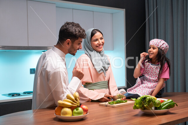  قضاء أوقات ممتعة مع الأبناء، ايماءات السعادة والسرور بالتعاون بين افراد العائلة داخل المطبخ, أم عربية خليجية سعودية محجبة تقوم بتعليم ابنتها الطبخ، مهارات وفنون الطبخ والتقطيع, مفهوم النظام الغذائي الصحي، إعداد وتحضير الطعام بمكونات طبيعية طازجة