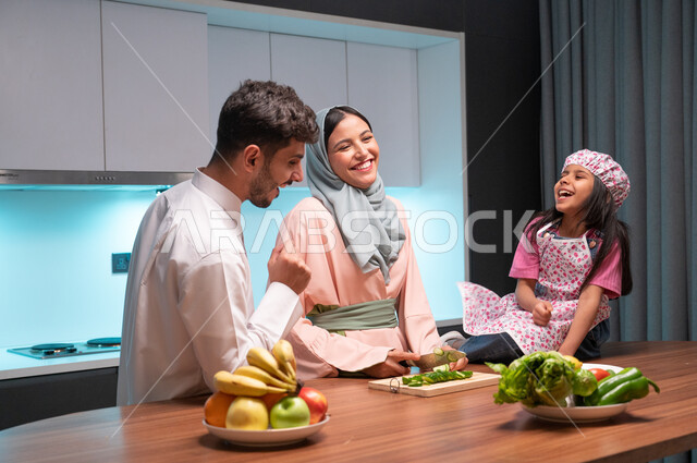 مفهوم النظام الغذائي الصحي، قضاء أوقات ممتعة مع الأبناء، مهارات وفنون الطبخ والتقطيع, ايماءات السعادة والسرور بالتعاون بين افراد العائلة داخل المطبخ, أم عربية خليجية سعودية محجبة تقوم بتعليم ابنتها الطبخ، إعداد وتحضير الطعام بمكونات طبيعية طازجة
