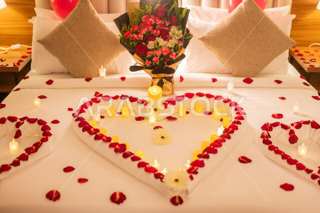 احتفالات بذكرى الزواج، صورة مقربة لسرير مزين بالشموع والورود الحمراء على شكل قلب للاحتفال بيوم الفلنتاين، الاهتمام بالمناسبات الخاصة، تزيين غرفة النوم بطريقة رومانسية، مشاعر الحب والود، مفهوم الارتباط والإلفة.