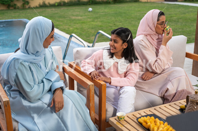 مشاركة الابناء في الاحاديث والدردشات، قضاء أوقات ممتعه في أحد المنتجعات، عائلة عربيه خليجيه سعودية تجلس في إحدى الشاليهات للتسليه والترفيه، أجواء أسرية مليئة بالحب، التسامر والضحك مع الافراد، تناول المشروبات الساخنه  في الهواء الطلق