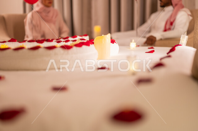 Hanging out and exchanging conversations between spouses, decorating the bedroom in a romantic way, wedding anniversary celebrations, a close-up picture of a bed decorated with candles and red roses in the shape of a heart to celebrate Valentine’s Day, interest in special occasions, feelings of love and affection, the concept of connection and familiarity