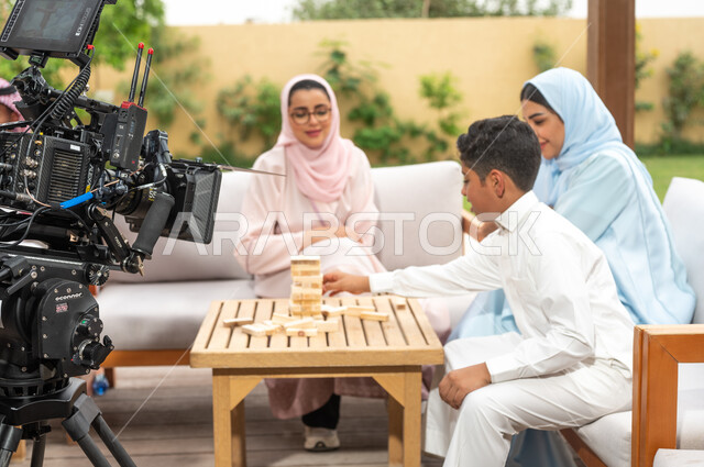 ألعاب مسلية لتنمية مهارات التفكير والذكاء عند الأطفال، الاستمتاع في العطلة الصيفية في إحدى المنتجعات، خلف الكواليس لجلسة تصوير لعائلة عربية خليجية سعودية تلعب لعبة جينغا في الهواء الطلق، رص الألواح الخشبية، لقطة مقربة لكاميرا حديثة ومطورة.