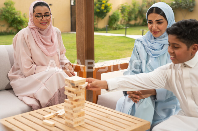 الاستمتاع والسرور بالأنشطة العائلية، قضاء أوقات ممتعة مع الأبناء في الإجازة الصيفية في إحدى المنتجعات، ألعاب مسلية لتنمية مهارات التفكير والذكاء عند الأطفال، عائلة عربية خليجية سعودية تلعب لعبة جينغا في الهواء الطلق، رص الألواح الخشبية.