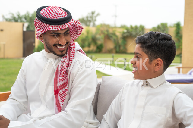 الاهتمام والاعتناء بالجانب النفسي للأبناء ،صورة مقربة لأب عربي خليجي سعودي يرتدي الزي التقليدي برفقة ابنه في إحدى الشاليهات، الضحك والتسامر مع الأولاد، قضاء عطلة نهاية الاسبوع في الخارج، الاستمتاع بالأجواء الصيفيه في التنزه في الهواء الطلق