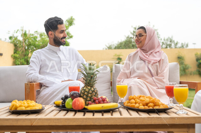 مفهوم العلاقات الزوجية الناجحة السعيده ،أطباق الفواكه المتنوعه والعصائر الطبيعيه المنعشة على الطاولة، الاستمتاع في أوقات الفراغ في أحد الشاليهات، التنزه في الهواء الطلق ،زوجان عربيان خليجيان سعوديان يقومان بتبادل الأحاديث والدردشات، اجواء مليئة بالمحبة والود