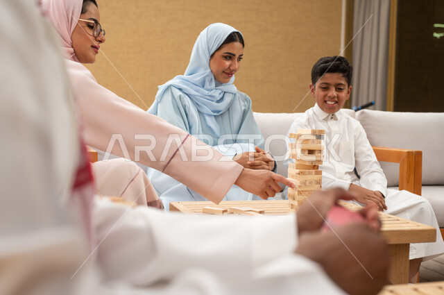 المتعة والسعادة في أحد الشاليهات في العطلة الصيفية، ممارسة الأنشطة والألعاب الجماعية المسلية لتنمية مهارات التفكير والذكاء، عائلة عربية خليجية سعودية تلعب لعبة جينغا في الهواء الطلق، صورة مقربة لرجل خليجي سعودي يلعب لعبة الورق