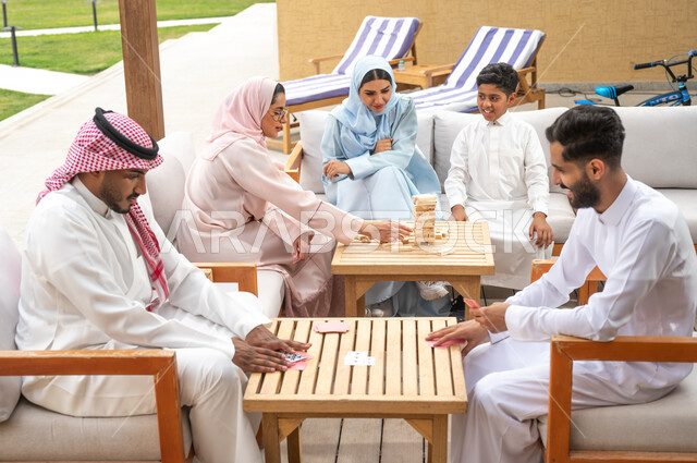ألعاب مسلية لتنمية مهارات التفكير والذكاء، الاستمتاع والسرور بالأنشطة العائلية الجماعية، قضاء أوقات ممتعة في الإجازة الصيفية في إحدى المنتجعات، عائلة عربية خليجية سعودية تلعب لعبة جينغا في الهواء الطلق، رجلان سعوديان يلعبان لعبة الورق، مفهوم التركيز والتحدي.