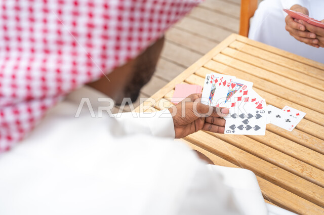  قضاء وقت ممتع في ممارسة الأنشطة والألعاب المسلية، المتعة والسعادة في أحد الشاليهات في العطلة الصيفية، صورة مقربة لرجلين عربيين خليجيين سعوديين يلعبان لعبة الورق، مفهوم التركيز والتحدي في لعب الشدة