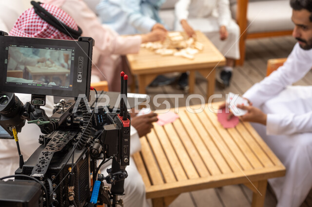 قضاء أوقات ممتعة مع الأهل والأصدقاء في الإجازة الصيفية، أنشطة ترفيهية وألعاب مسلية، خلف الكواليس لجلسة تصوير لعائلة عربية خليجية سعودية تلعب لعبة جينغا في الهواء الطلق، رص الألواح الخشبية، لقطة مقربة لكاميرا حديثة ومطورة، رجلان عربيان سعوديان يلعبان لعبه الورق.