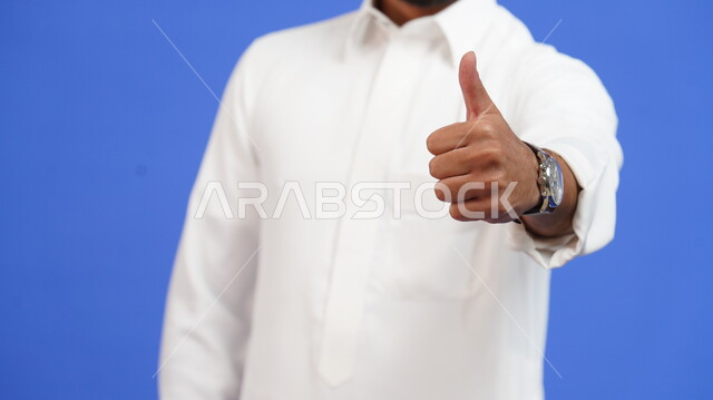 إشارات حركات الاعجاب والقبول والموافقة, بورتريه مقرب لرجل عربي خليجي سعودي يرتدي الثوب التقليدي يرفع اصبع الابهام للأعلى بإيماءات علامة الجودة والرضا، خلفية زرقاء