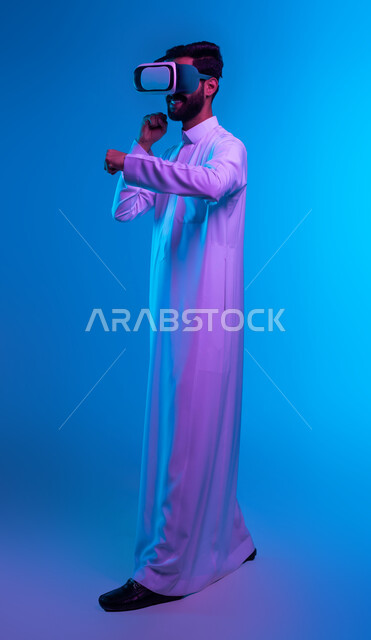 Discharging negative energy, practicing self-defense using technological techniques, practicing combat movements through video games, a side portrait of a Saudi Gulf Arab young man wearing a traditional dress and virtual reality glasses with boxing and wrestling gestures, full body portrait, blue background