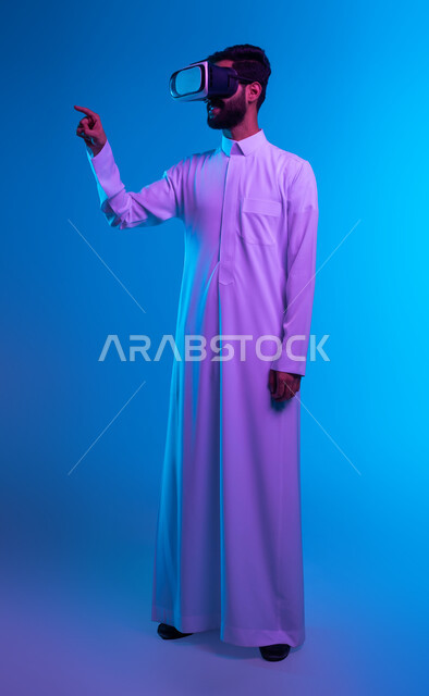 Simulating the imaginary world, touch and pressure movements, a portrait of a Saudi Gulf Arab man wearing a traditional thobe and 3D VR glasses, standing straight and pointing with his index finger at something he is watching in virtual reality, click signals on a holographic screen, full body image, blue background