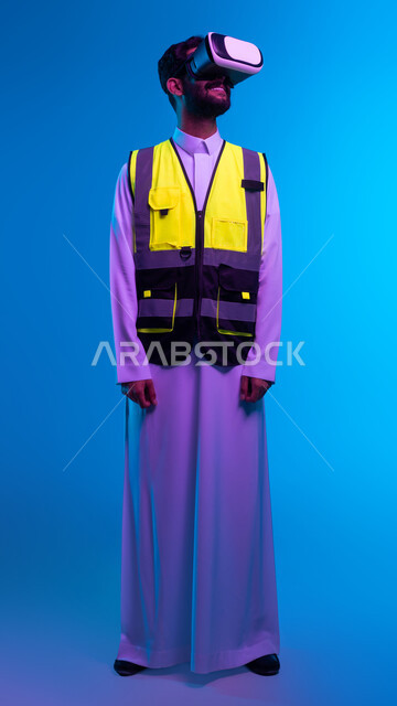 نمو وتطور المجال الهندسي، محاكاة الواقع الخيالي والافتراضي، التقدم التكنولوجي في الهندسة المعمارية، رؤية مستقبلية 2030، بورتريه من الخلف لمهندس عربي خليجي سعودي مبتسم يرتدي سترة العمل ونظارة الفي آر ثلاثية الأبعاد، صورة الجسم بالكامل، خلفية زرقاء