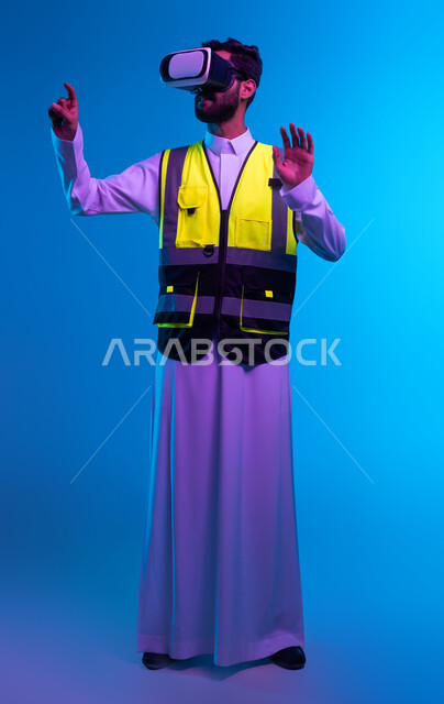 تطور المجالات الهندسية عبر نظارات الفي آر، رؤية مستقبلية سعودية 2030، التفاعل مع الهندسة الافتراضية، بورتريه لمهندس عربي خليجي سعودي يرتدي السترة الخاصة بالعمل ونظارة الواقع الافتراضي يقوم بالنقر على عنصر ما، صورة لكامل الجسم، خلفية زرقاء