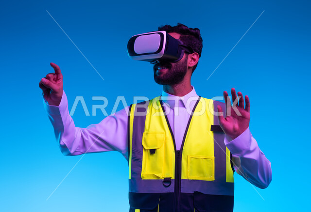 Growth and development of the engineering field, simulation of imaginary and virtual reality, technological progress in architecture, future vision 2030, close-up portrait of a smiling Saudi Arabian Gulf engineer wearing a work jacket and 3D VR glasses, clicking on an element, blue background