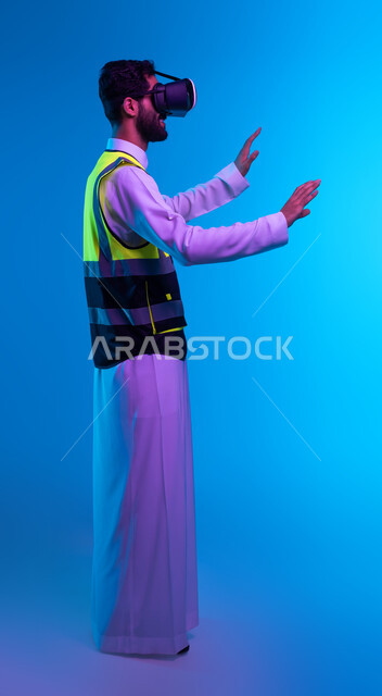 Tor and technological progress in architecture, future vision 2030, simulation of imaginary reality, interaction with virtual engineering fields, portrait from the side of a Saudi Gulf Arab engineer wearing a work jacket and VR glasses trying to touch an element, full body image, blue background