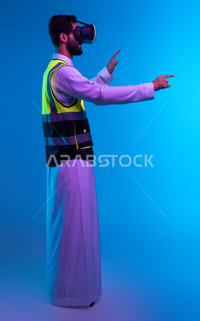 Tor and technological progress in architecture, future vision 2030, simulation of imaginary reality, interaction with virtual engineering fields, portrait from the side of a Saudi Gulf Arab engineer wearing a work jacket and VR glasses trying to touch an element, full body image, blue background