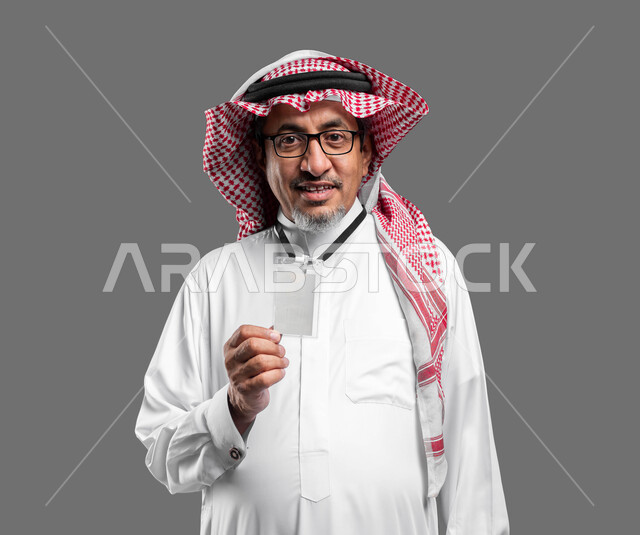 موك اب بطاقة تعريفية مفرغة باللون الابيض، بورتريه مقرب لرجل عربي خليجي سعودي كبير بالسن مبتسم يرتدي الشماغ والثوب التقليدي ونظارة طبية يضع هوية شخصية، رجل اعمال يرتدي بادج شخصي، النظر الى الكاميرا بايماءات السعادة والسرور، خلفية رمادية