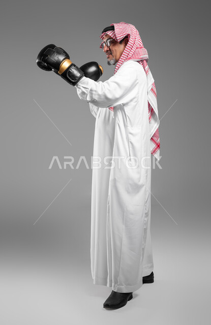 Practicing martial movements, increasing muscle endurance, a portrait of an elderly, smiling Saudi Arabian Gulf man wearing gloves learning the arts of boxing, maintaining physical fitness, enhancing bone and joint health, full-length body image, gray background