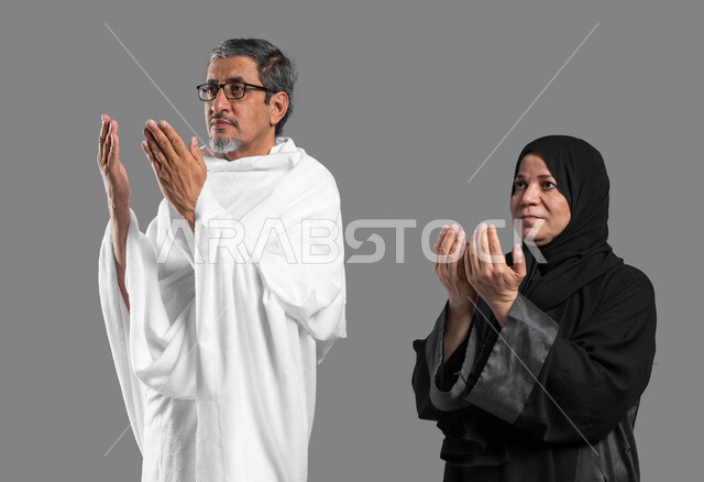 المحافظة على الدعاء وطلب المغفرة من الله تعالى, فضل العمرة في شهر رمضان المبارك, تلبية نداء الله لاداء فريضة الحج، بورتريه مقرب لزوجين عربيين خليجيين سعوديين كبيرين بالسن يرتديان ثياب الإحرام يدعوان بخشوع وتضرع، اسلاميات وعبادة، خلفية رمادية.