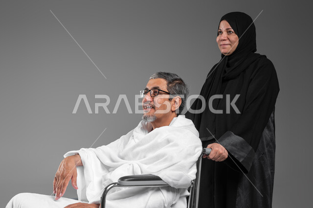 السفر لاداء فريضة الحج في شهر ذو الحجه، بورتريه مقرب لرجل وامرأة عربيين خليجيين سعوديين يرتديان ملابس الاحرام يستعدان للعمره في شهر رمضان المبارك، مساعدة ذوي الاحتياجات الخاصه وكبار السن, مفهوم حسن المعاشره  في الحياه الزوجيه, خلفيه رماديه
