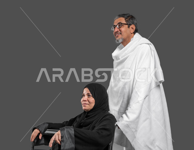 السفر للعمره في شهر رمضان المبارك، بورتريه مقرب لرجل وامرأة عربيين خليجيين سعوديين يرتديان ملابس الاحرام يستعدان لاداء فريضة الحج في شهر ذو الحجه, مساعدة ذوي الاحتياجات الخاصه وكبار السن, مفهوم حسن المعاشره  في الحياه الزوجيه, خلفيه رماديه