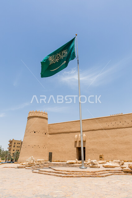 معالم الرياض التراثية، العلم السعودي وراية الوطن امام متحف قصر المصمك التاريخي في مدينة الرياض في وضح النهار، فن الهندسة المعمارية والمباني الطينية القديمة، اماكن اثرية سياحية في المملكة العربية السعودية