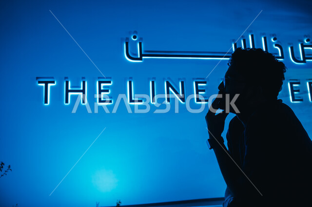 الديكورات الداخلية في اقسام المعرض، رجل عربي خليجي سعودي يقف أمام شعار "ذا لاين" في الرياض بإيماءات التفكير، التخطيط المعماري لقطاع العقارات، الابتكارات المستقبلية في البنية التحتية للمدن الذكية، رؤية سعودية مستقبلية 2030، بناء مستقبل حضاري متطور في المملكة